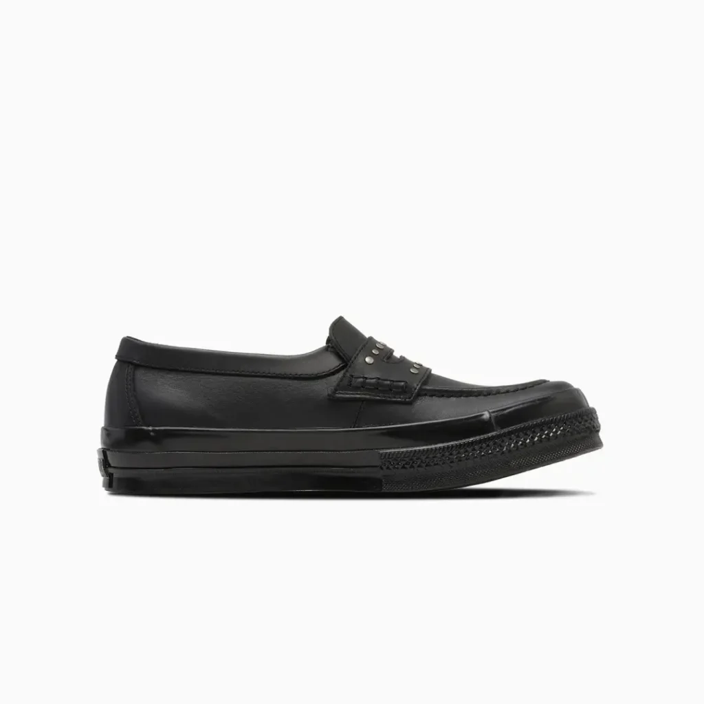 Opposite lateral side of the black Converse penny loafer, emphasizing the streamlined leather upper, low-cut silhouette, and monochrome black shoe