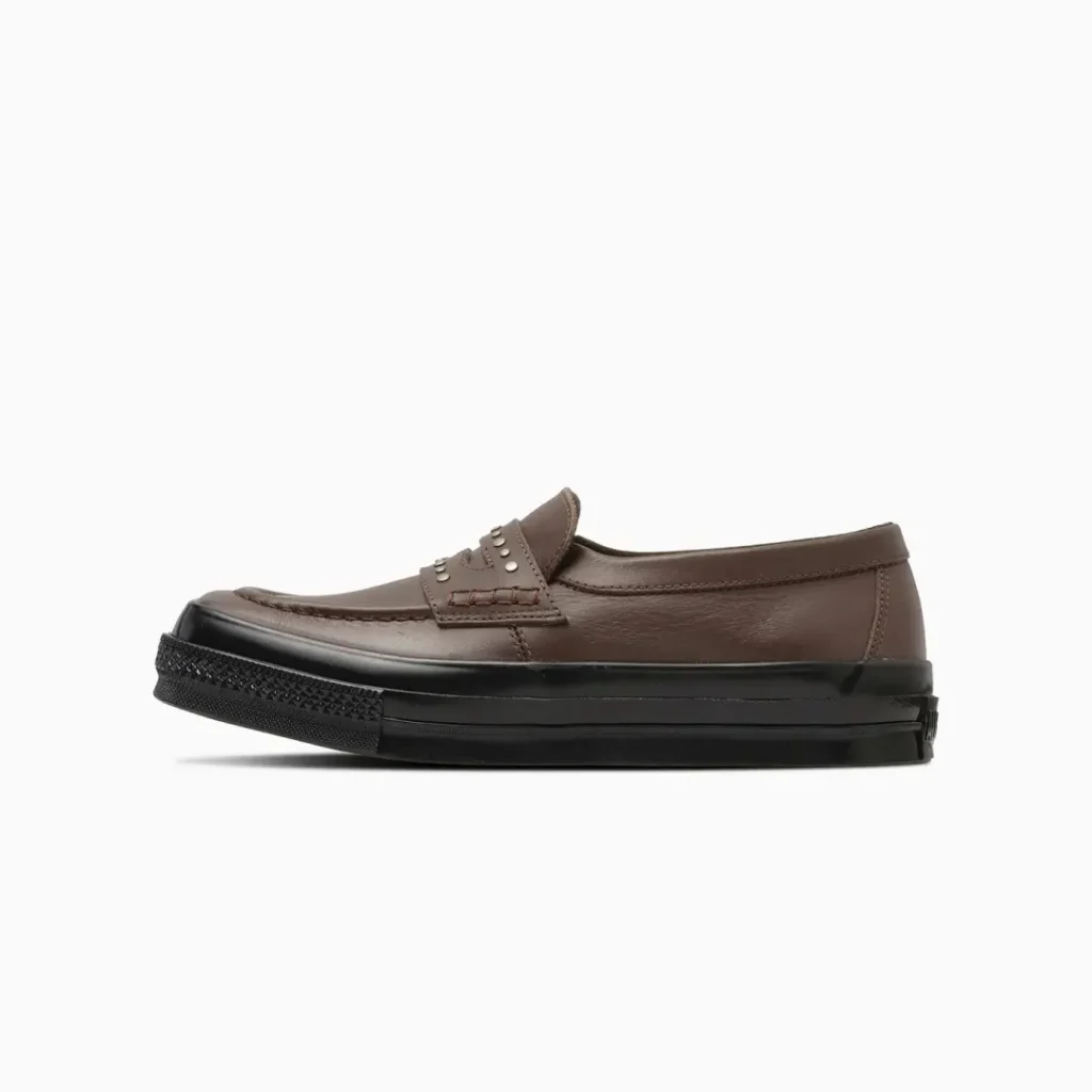 Side view of the brown Converse penny loafer with smooth brown leather, square moc toe, silver studded penny strap, and contrasting black rubber sole
