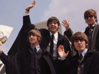 The Beatles pose and wave to fans during the height of Beatlemania, featuring John Lennon, Paul McCartney, George Harrison, and Ringo Starr in classic 1960s attire as they greet crowds from an airport arrival platform