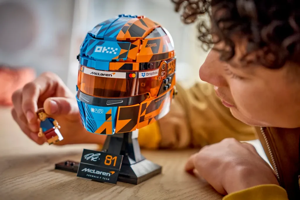 Close-up of the LEGO Oscar Piastri helmet showcasing the blue-and-papaya McLaren livery, tinted visor, sponsor details, and accompanying driver minifigure