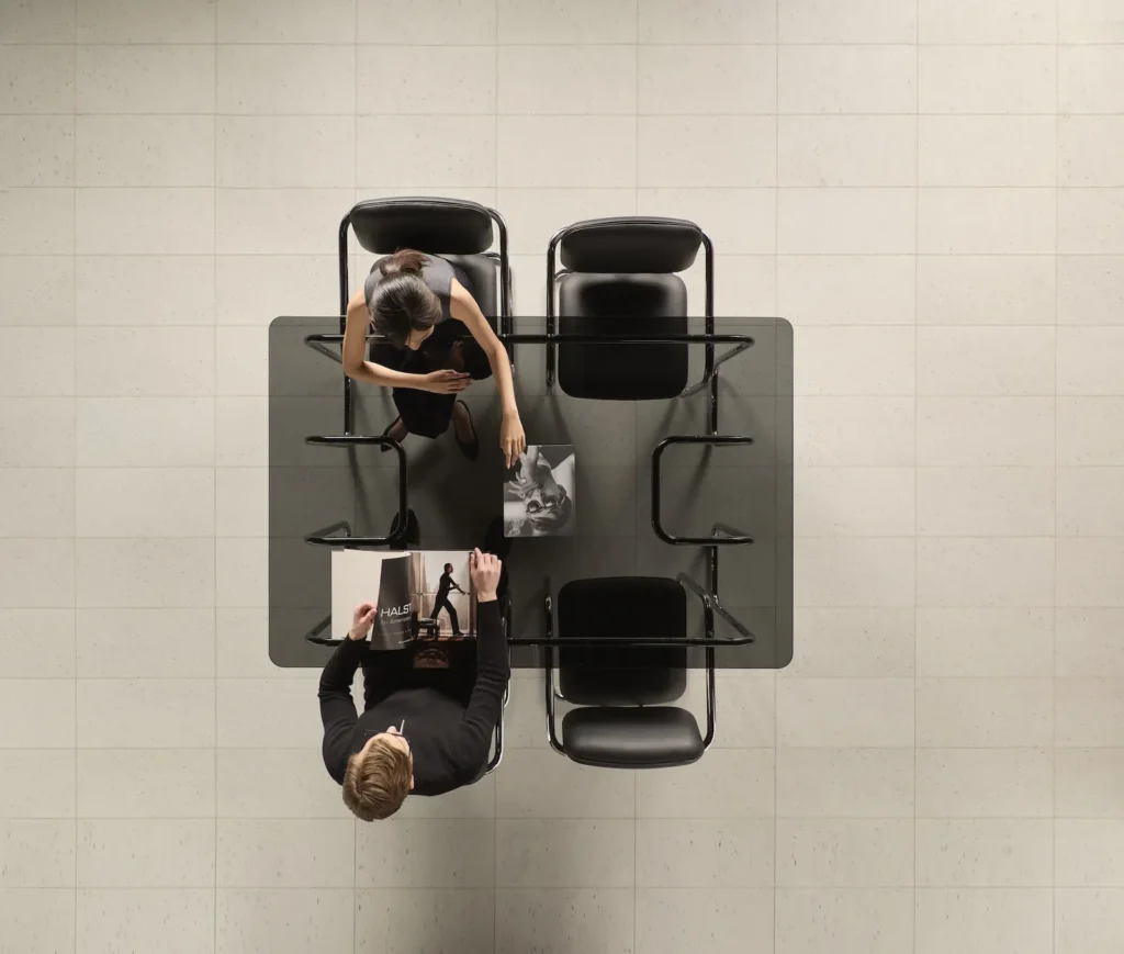 Overhead view of SOM79 chairs around a glass table in a minimalist modern office, evoking Halston’s iconic Olympic Tower atelier with sleek chrome frames and black leather upholstery