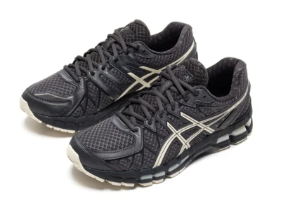 Pair of ASICS GEL-KAYANO 20 shoe displayed in a three-quarter studio view. The silhouette combines charcoal mesh, black structural overlays, silver ASICS stripes, and segmented GEL cushioning for a technical running-inspired aesthetic