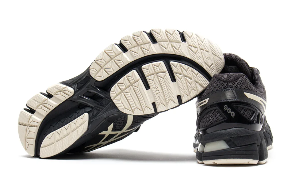 Outsole-focused product image displaying the segmented traction pattern and flex-groove construction of the GEL-KAYANO 20. Cream-colored rubber sections contrast against the black midsole and stability frame, showcasing the shoe’s performance-driven foundation