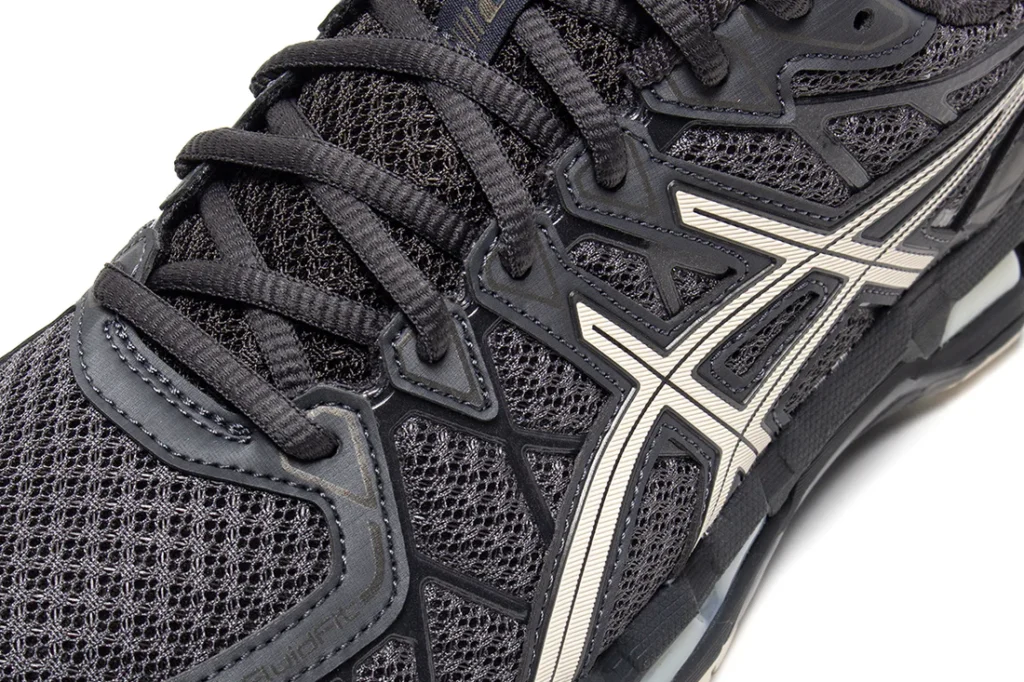 Close-up detail of the lateral side panel showcasing the breathable open-weave mesh upper, layered synthetic cage construction, and metallic silver ASICS logo. The image highlights the shoe’s engineered support system and intricate panel