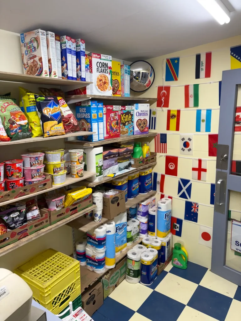Interior view of the completed store stocked with cereals, snacks, household goods, and international products, with small national flags decorating the walls above the shelve
