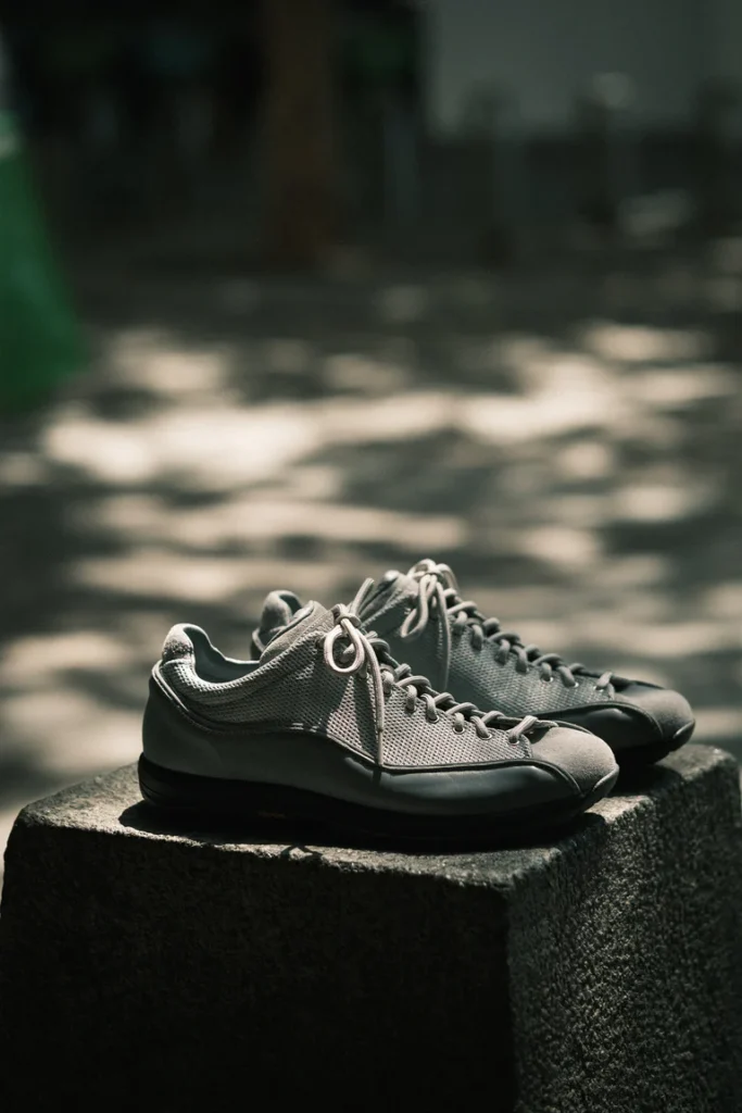 Pair of gray low-top DIEMME sneakers with breathable mesh uppers and black Vibram soles displayed on a concrete pedestal in natural sunlight, photographed with a shallow depth of field