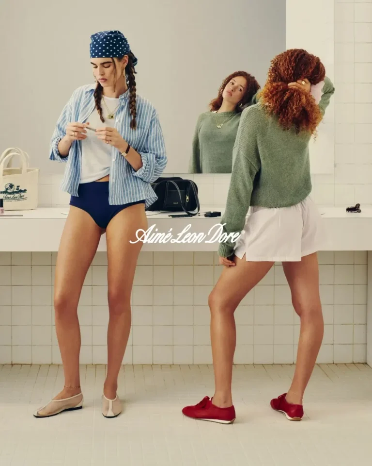 Two models in a dressing-room setting wearing Aimé Leon Dore spring essentials, including striped shirts, knitwear, briefs, shorts, and ballet flats