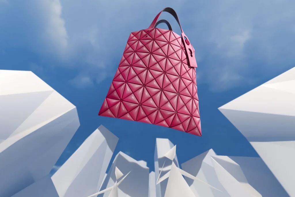 Vibrant pink geometric tote bag hovers against a bright blue sky framed by abstract white architectural forms. The bold color and iconic triangular pattern emphasize the collection’s play yet futuristic aesthetic