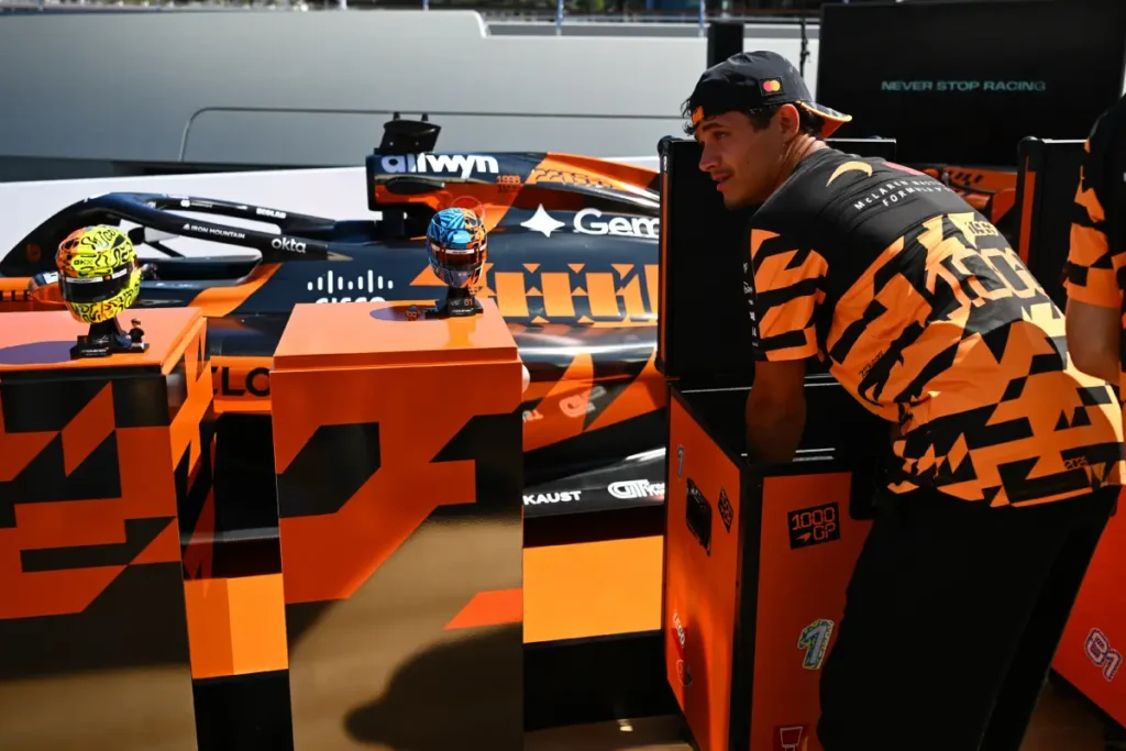 McLaren Formula 1 driver examining LEGO helmet display models beside a McLaren race car during a special promotional showcase event
