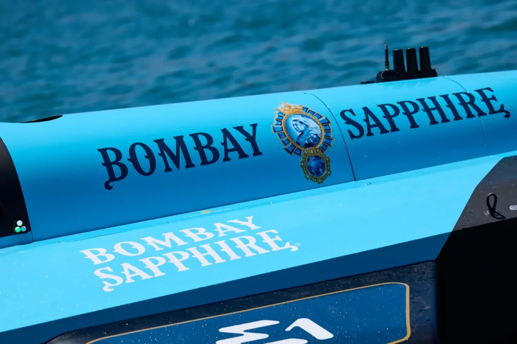 A chilled Bombay Sapphire gin bottle and ready-to-drink gin and tonic cans sit nestled among ice cubes. The vibrant blue packaging and frosted surfaces emphasize refreshment and premium cocktail culture