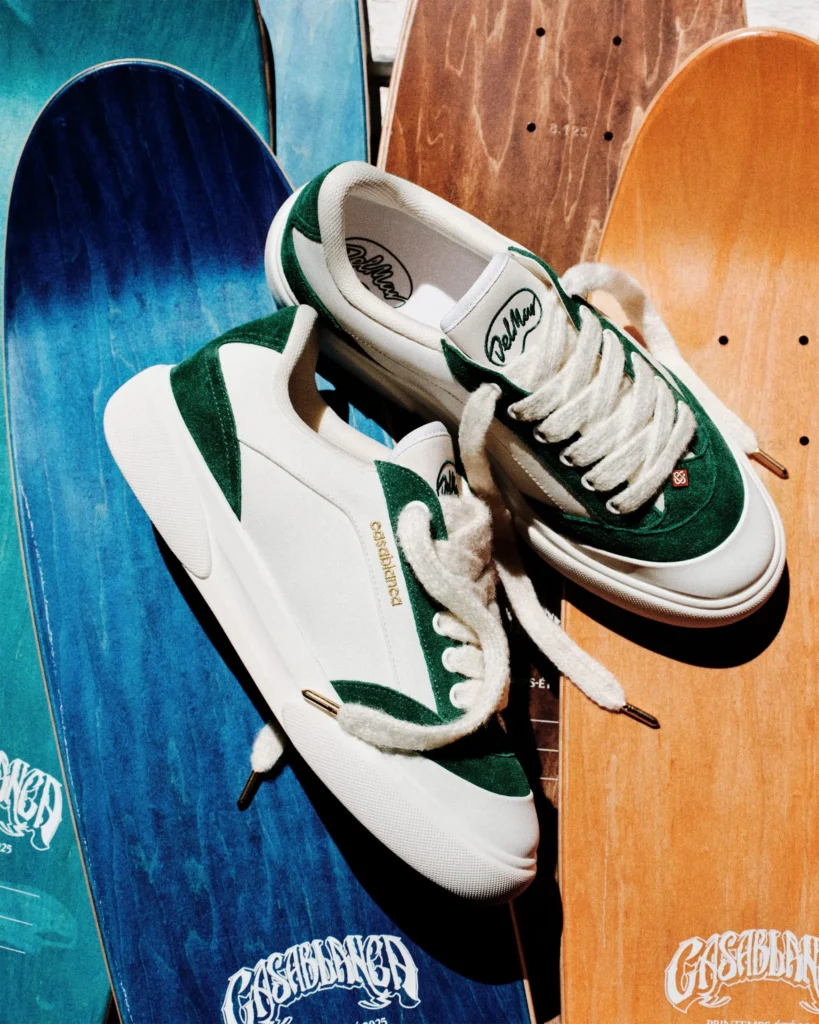 White-and-green Casablanca Del Mar shoe displayed on colorful skateboard decks, emphasizing premium suede overlays, gold Casablanca branding, and oversized laces against vibrant blue and woodgrain background