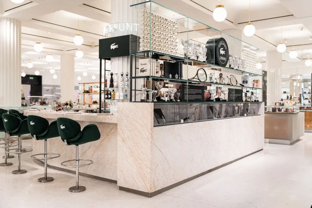 Wide view of the Club Lacoste bar installation with green velvet crocodile-branded stools, marble surfaces, trophy displays, and tennis-inspired décor creating an elevated retail hospitality experience