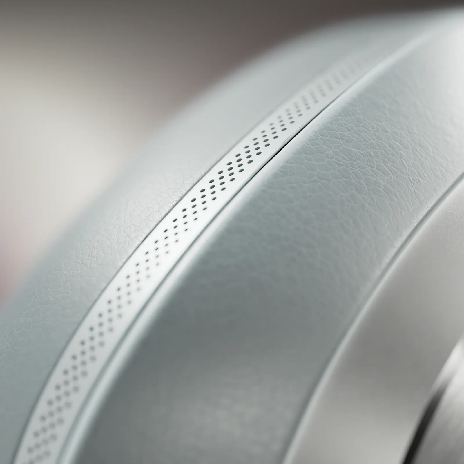 Extreme close-up of the headphone headband, highlighting perforated detailing and a textured leather-like surface in a pale gray colorway