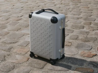 Silver Louis Vuitton Horizon aluminum carry-on suitcase displayed on a cobblestone street, emphasizing its embossed Monogram surface, durable construction, and minimalist luxury appeal