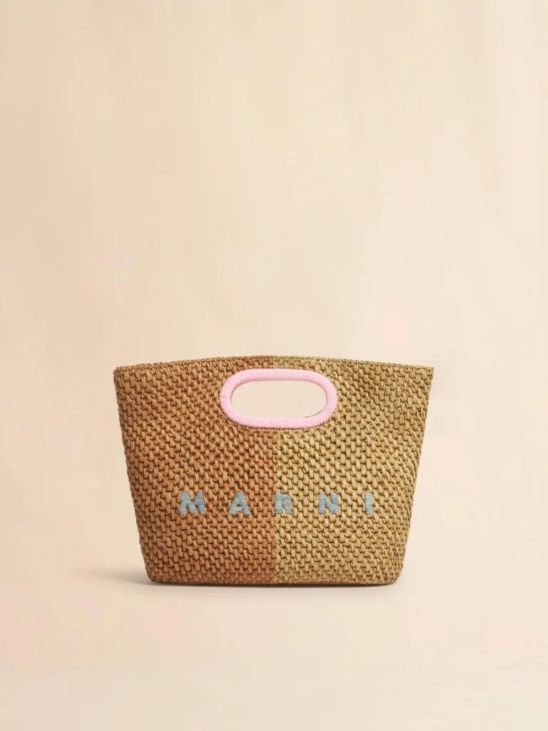 A woven Marni tote in contrasting tan and natural raffia shades with a soft pink embroidered handle opening. Grey logo lettering and a minimalist silhouette highlight the bag’s handcrafted texture