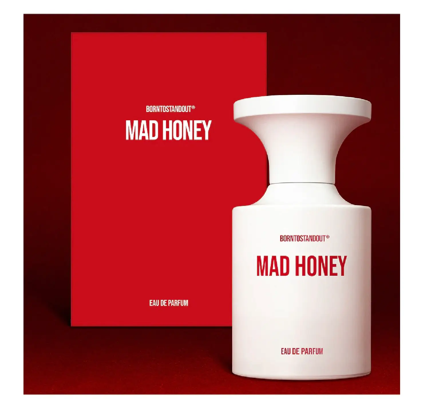BORNTOSTANDOUT® MAD HONEY Eau de Parfum displayed beside its matching red presentation box. The matte white bottle with vivid red lettering stands against a rich red backdrop, emphasizing the fragrance’s bold, modern, and graphic packaging design