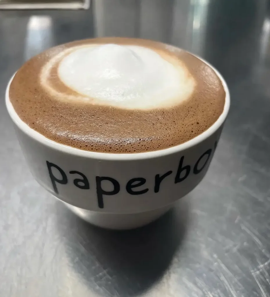 Close-up of a creamy cappuccino topped with thick milk foam, served in a white Setinn-branded cup on a stainless-steel café counter