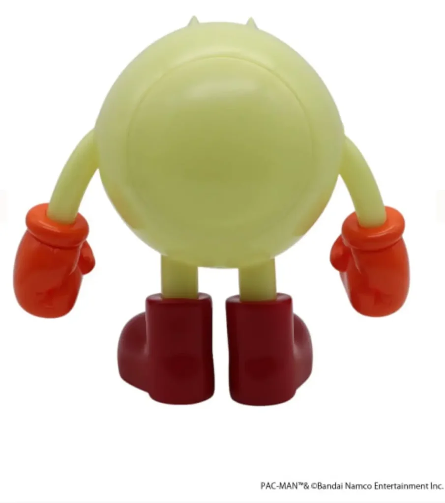 Rear view of the PAC-MAN collectible figure showing its translucent glow-in-the-dark body, rounded silhouette, curved arms, red boxing-style gloves, and oversized red boots. Small sculpted details on top of the head are view from the back