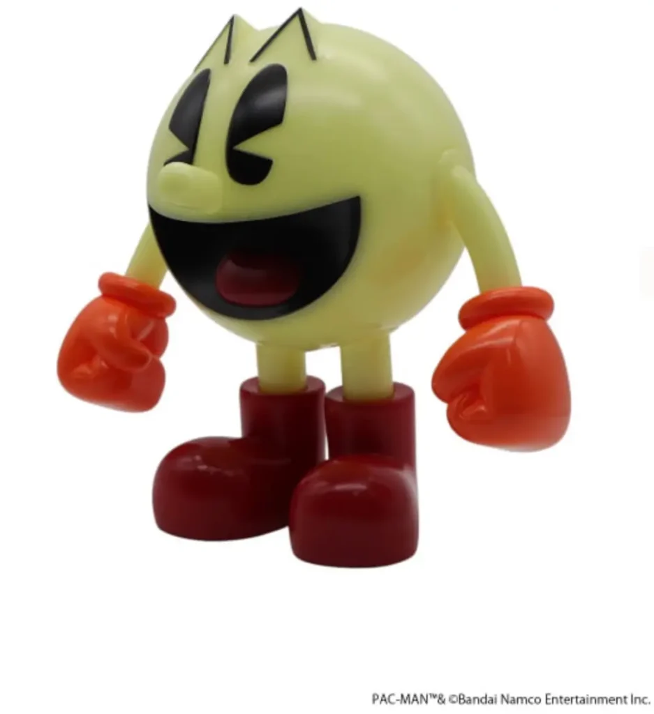 Three-quarter front view of the PAC-MAN figure posed with both gloved fists raised in celebration. The translucent yellow-green body, black facial features, and glossy red gloves and boots highlight the toy’s play arcade-inspired design