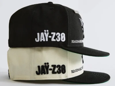 Two structured Paper Planes snapback caps are stacked against a clean white background, showcasing black and cream colorways. Both feature oversized embroidered “JAY-Z30” branding across the front panel, “REASONABLE DOUBT” embroidery on the side, flat brims with green undervisors, and premium stitched construction that celebrates the 30th anniversary of Jay-Z's landmark debut album