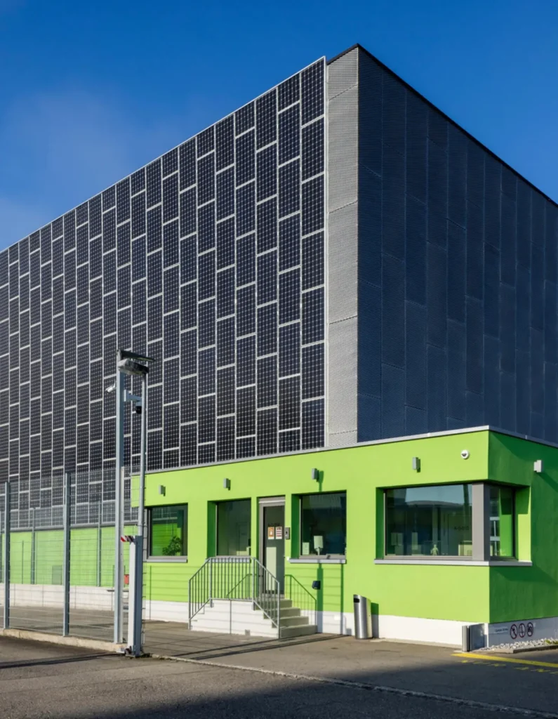 Modern data center facility with a solar-panel-clad exterior, bright green administrative offices, and secure perimeter fencing, showcasing sustainable digital infrastructure and renewable energy integration