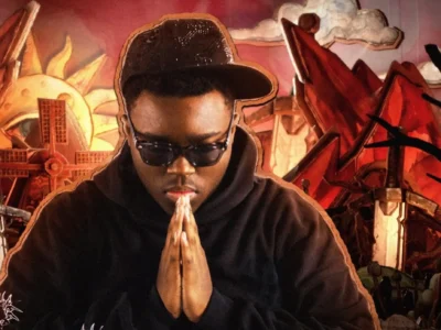 Slayr in signature sunglasses and black hoodie, hands in prayer pose, against dramatic red-hued BloodLuxe backdrop with swords and surreal architecture — official visual from “Eyesight” track