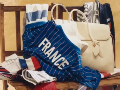 Jacquemus x Nike x FFF collection displayed on a wooden chair, featuring a blue pinstriped FRANCE jersey, tricolor apparel, white leather bag, striped accessories, and white sneakers inspired by French football heritage