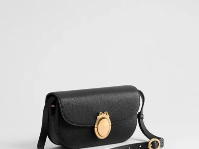 Three-quarter view of the Small Dior Médaillon Flap Bag in black grained calfskin, featuring a structured flap silhouette, adjustable leather shoulder strap, and a gold-tone Médaillon clasp inspired by Dior heritage motif