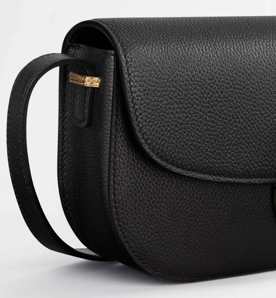 Detailed side profile of the Small Dior Médaillon Flap Bag emphasizing the rich grained calfskin texture, rounded structure, clean edge finishing, and decorative gold-tone hardware attachment