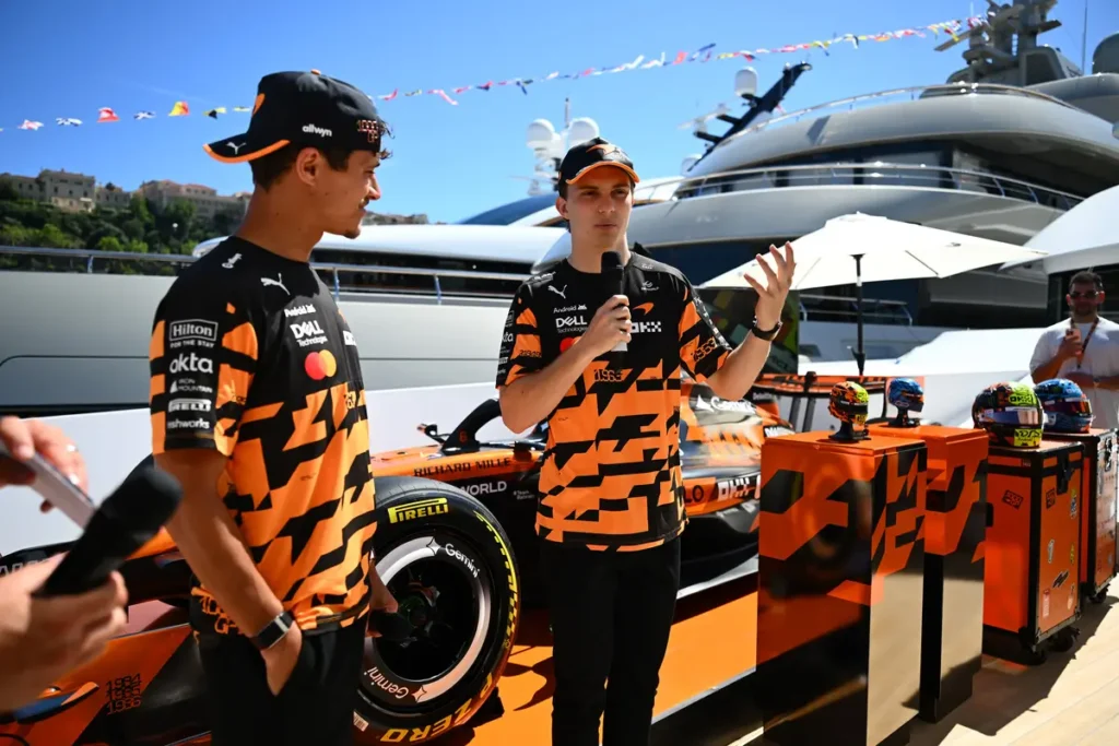 McLaren Formula 1 drivers speaking at a promotional event featuring LEGO helmet collectibles displayed alongside the team’s race car