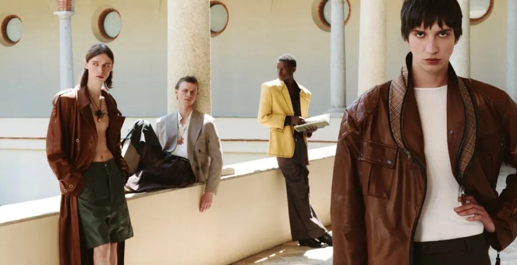 Editorial fashion campaign set within a sunlit Italian courtyard, showcasing models in leather outerwear, relaxed tailoring, layered accessories, and contemporary menswear inspired by classic European elegance