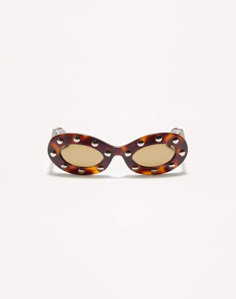 Valentino oval sunglasses in glossy tortoiseshell acetate featuring amber-tinted lenses and silver-tone stud embellishments surrounding each lens, shown from the front on a white backdrop