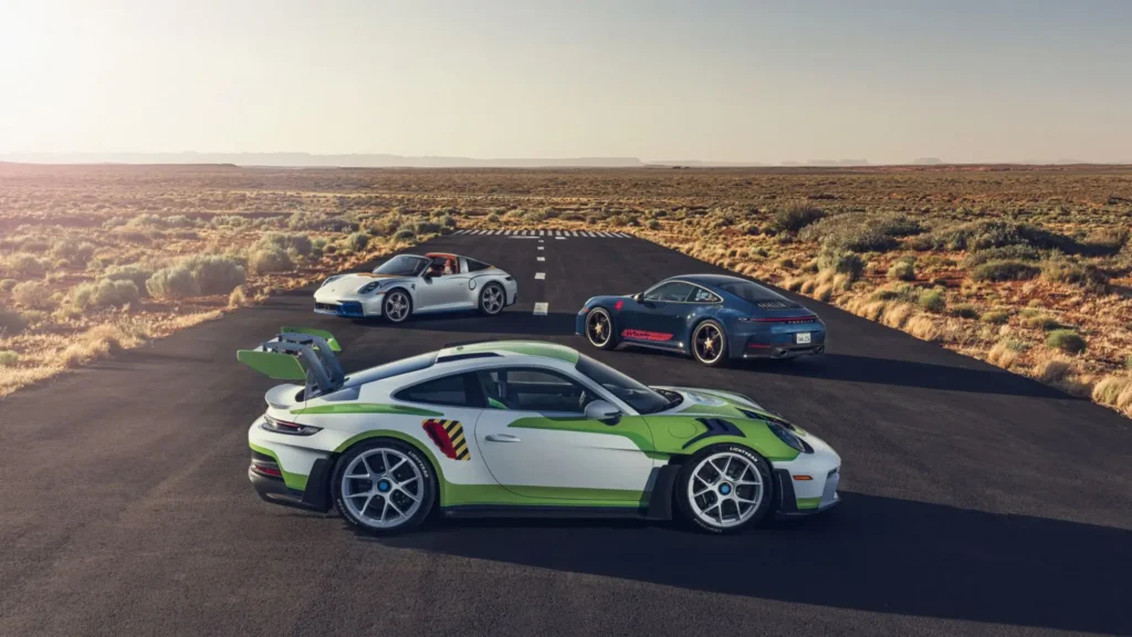 Three custom Porsche 911s inspired by Toy Story 5 — Buzz Lightyear GT3 RS, Woody roadster, and Jessie coupe — parked on a desert road under golden hour light, evoking a grown-up Hot Wheels fantasy. Porsche x Pixar collide