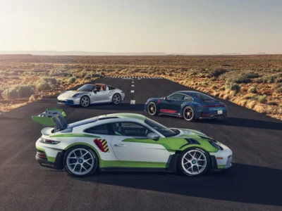 Three custom Porsche 911s inspired by Toy Story 5 — Buzz Lightyear GT3 RS, Woody roadster, and Jessie coupe — parked on a desert road under golden hour light, evoking a grown-up Hot Wheels fantasy. Porsche x Pixar collide