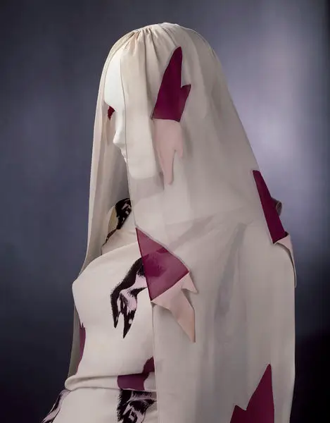 vant-garde mannequin draped in a translucent ivory veil adorned with pink and burgundy appliqué details, creating a mysterious and surreal couture present