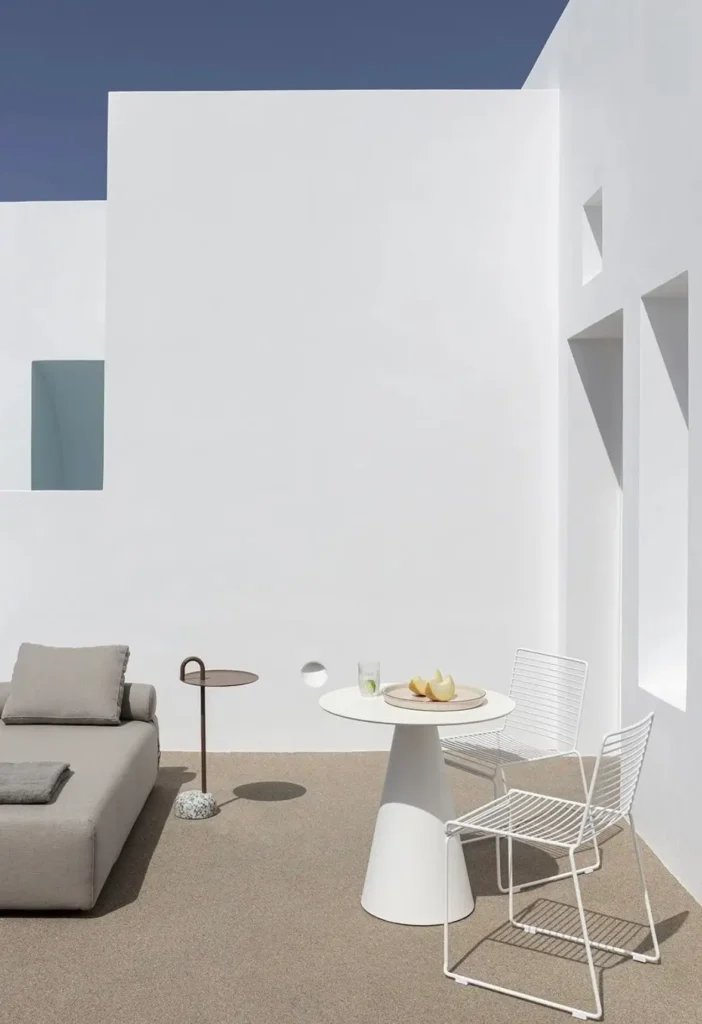 Minimal outdoor courtyard featuring sculptural white walls, contemporary furniture, and crisp geometric shadows that emphasize the purity of Cycladic-inspired architecture
