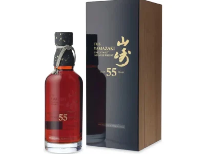 The Yamazaki 55 Years Old Single Malt Japanese Whisky displayed beside its luxury presentation box. The bottle showcases a rich mahogany-amber spirit, gold-embossed branding, and a handcrafted gold-flecked stopper, while the glossy black and wood-grain box highlights the exclusive aged expression