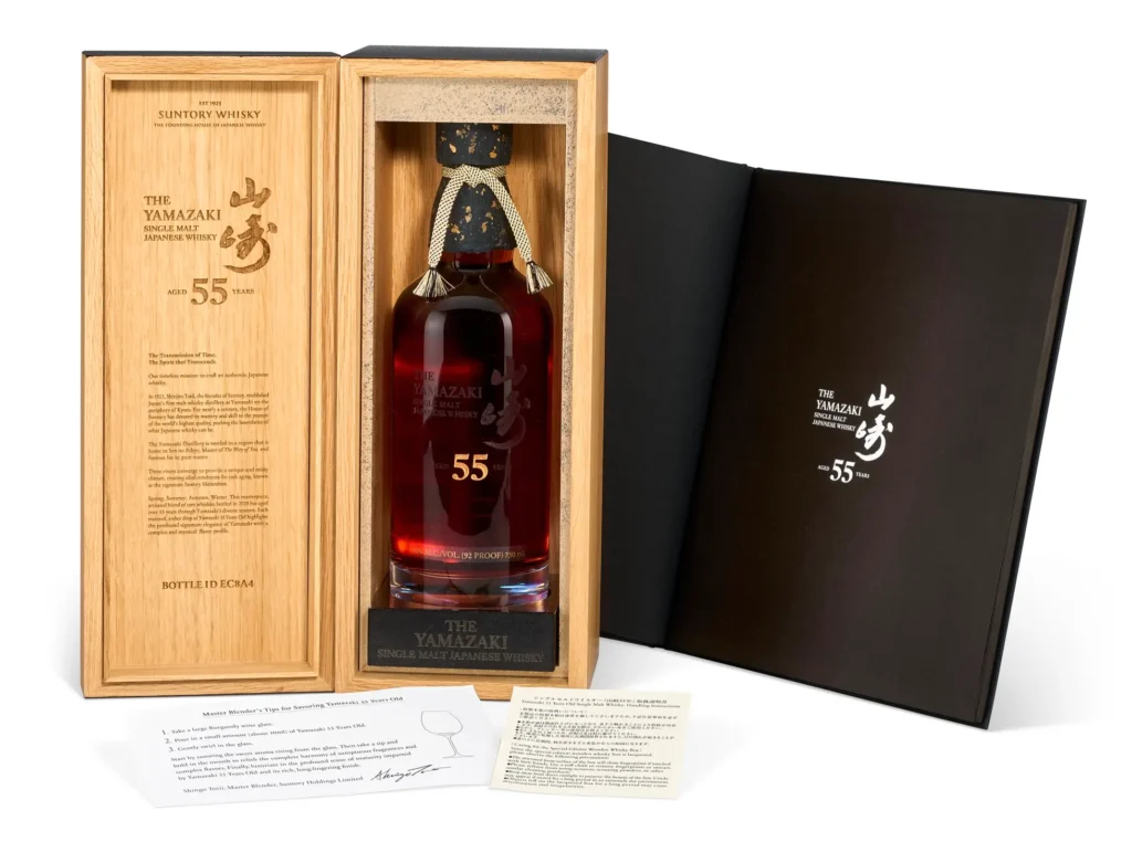The Yamazaki 55 Years Old whisky presented inside an open wooden collector’s case. The bottle rests in a custom-fitted compartment alongside engraved branding, informational inserts, and a black outer presentation cover, emphasizing the rarity and craftsmanship of the ultra-aged Japanese whisky release