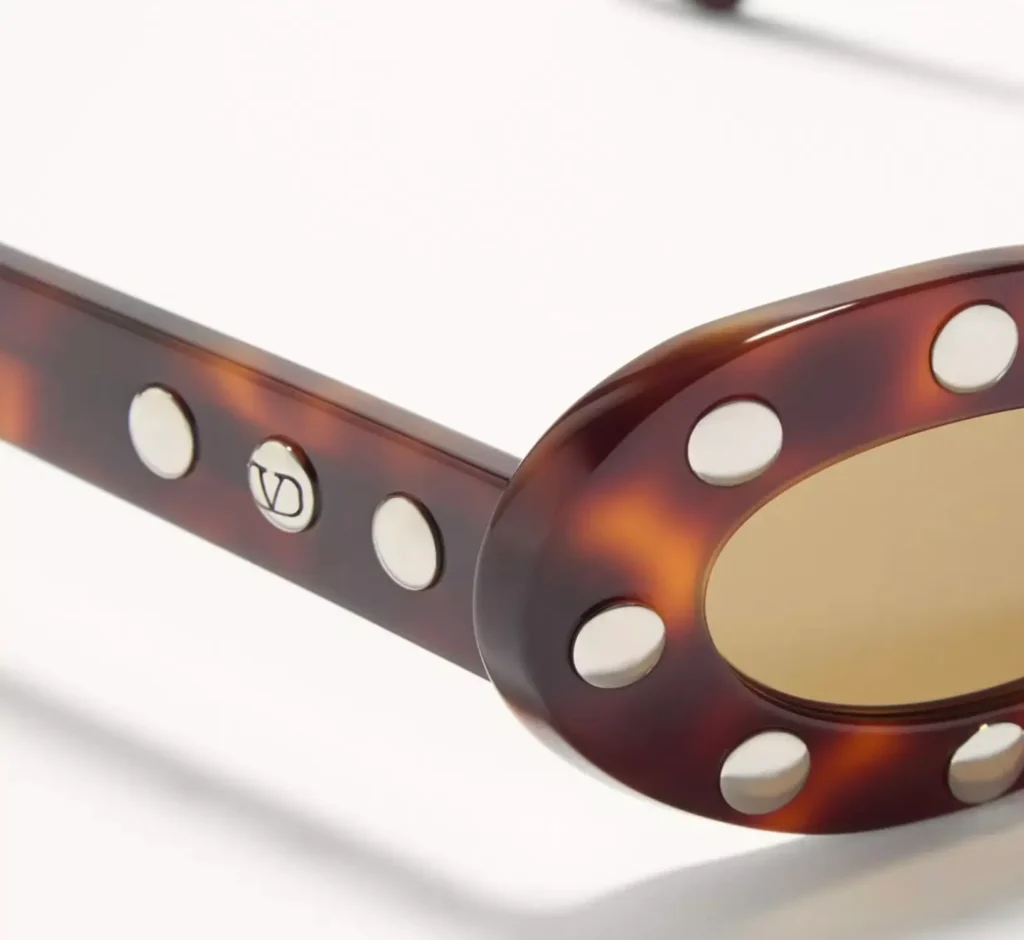Close-up of the sunglasses’ side arm and lens frame, highlighting the VLogo Signature hardware, tortoiseshell acetate construction, and silver stud detailing against a clean white background