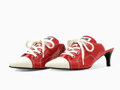 Pair of red patent leather mule heels styled with Converse All Star-inspired detailing, featuring oversized laces, mesh tongues, off-white toe caps, and elegant pointed sil