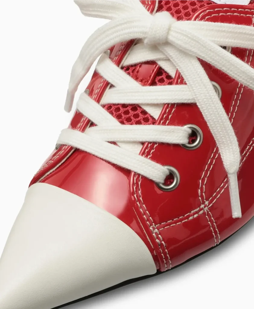 Close-up detail of the patent red upper showing oversized cream laces, metal eyelets, white contrast stitching, mesh tongue texture, and off-white pointed toe cap