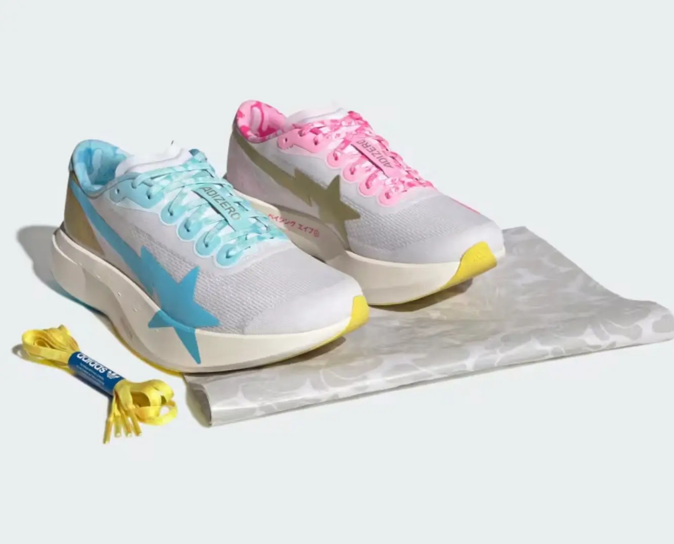 The blue and pink colorways are presented together beside extra yellow laces and folded camo wrapping paper, emphasizing the collaborative styling and complementary pastel tincture palette