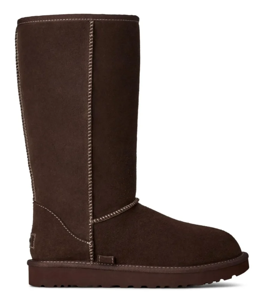 Side profile of a classic tall UGG boot crafted entirely in dark brown suede. Contrast whipstitch detailing traces the seams, while the clean silhouette and durable rubber sole maintain the brand’s signature winter style