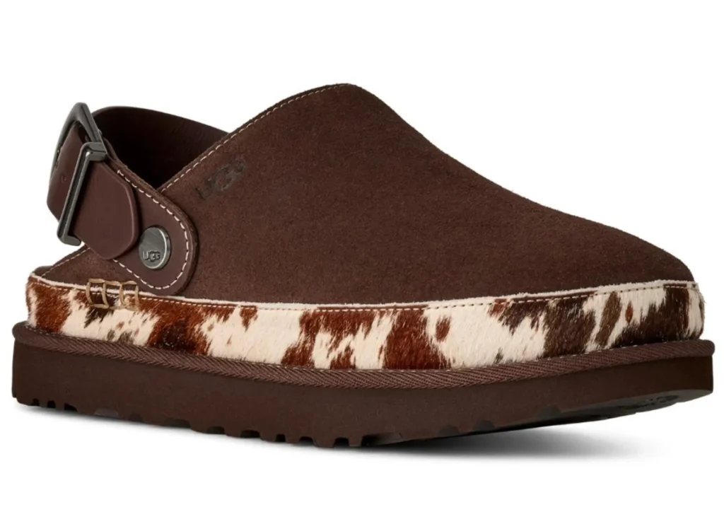 Three-quarter front view of a brown suede UGG slingback clog with an adjustable leather strap and silver buckle. The design features a rounded toe, cow-print calf hair midsole wrap, and thick rubber platform sole