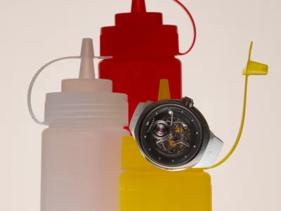 Vanguart watch displayed among translucent condiment squeeze bottles in red, white, and yellow. The futuristic timepiece rests atop a bright yellow bottle, blending haute horology with play diner-inspired imagery