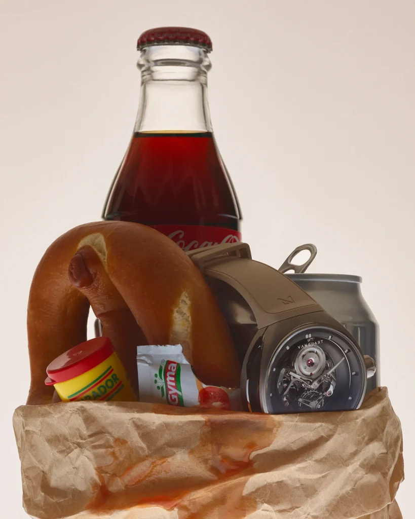 A Vanguart watch emerges from a paper grocery bag filled with a pretzel, soft drink bottle, canned beverage, condiments, and snacks. The composition merges everyday comfort foods with luxury design