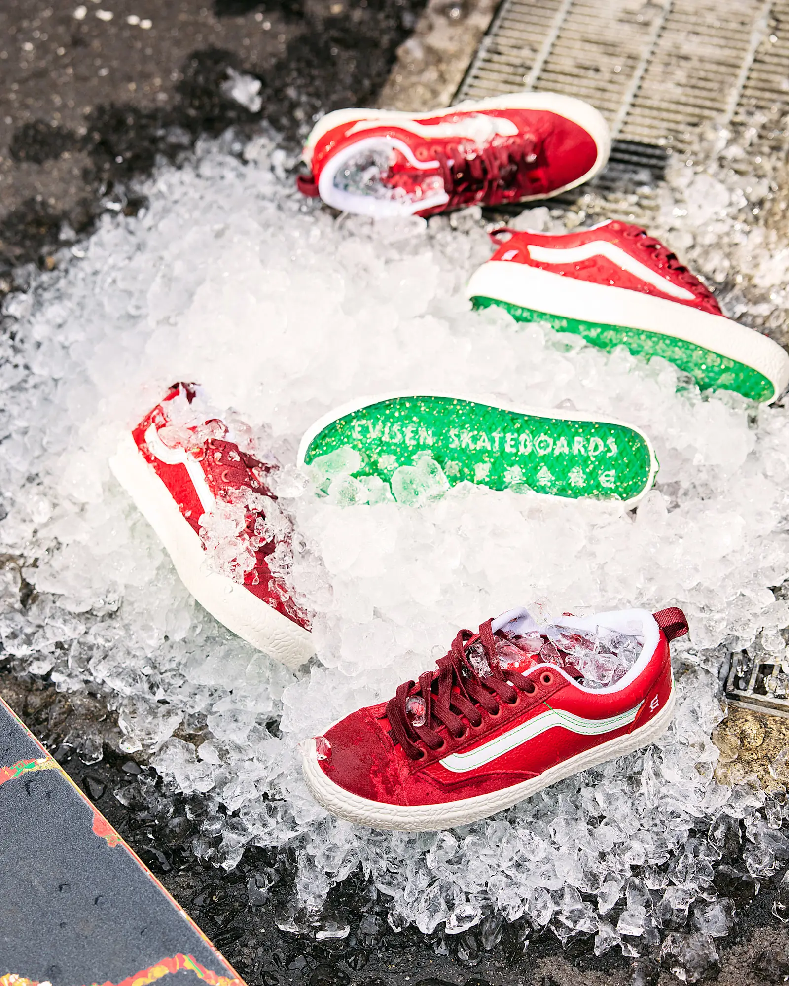 Vans Skate Old Skool 36+ Evisen Skateboards sneakers scattered across crushed ice outdoors, showcasing red uppers, white side stripes, and bright green translucent sole