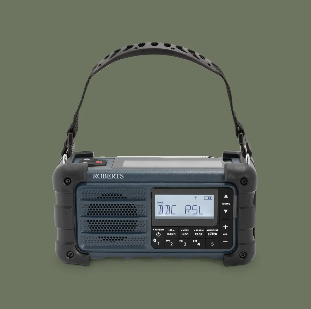 Front-facing studio shot of the compact emergency radio featuring a perforated speaker grille, monochrome LCD display, dedicated tuning controls, preset buttons, and durable corner protection. The navy-blue and black color scheme gives the radio a functional, industrial appearance suited for emergency preparedness and outdoor recreation
