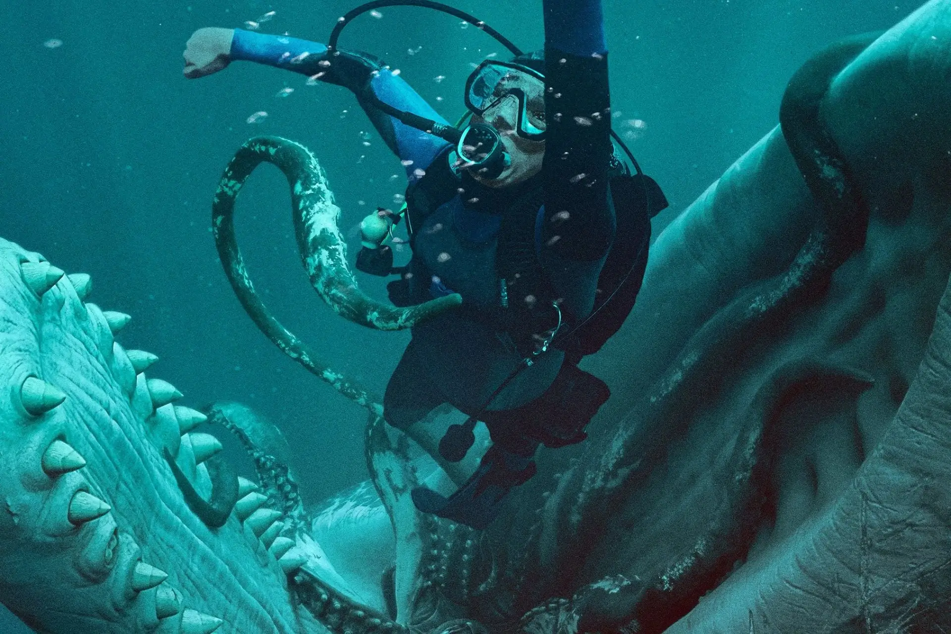 An underwater diver in full scuba gear swims through the open jaws of a colossal sea creature while massive tentacles coil around the scene. Suspended in blue-green water filled with bubbles, the diver appears dwarfed by the creature’s enormous teeth and twisting limbs, creating a dramatic, cinematic deep-sea survival moment