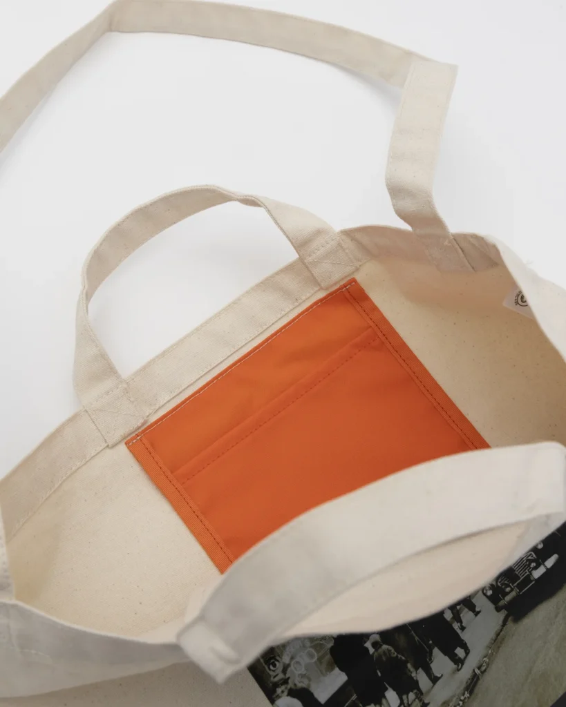 Interior view of the MOSCOT x BEAMS PLUS canvas tote bag revealing a vibrant orange utility pocket, showcasing practical storage details and durable construction
